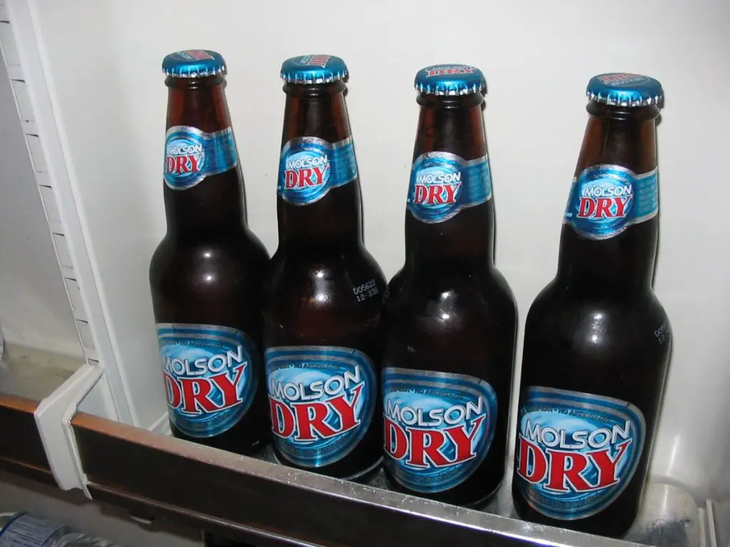 Four Bottles Of Molson Dry In A Fridge Rack.