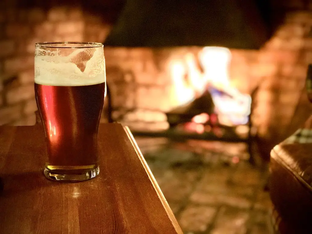 A Glass Of Ale On A Table By A Blazing Fire.